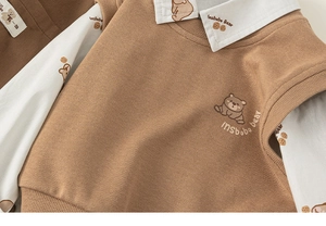 Detailed close-up of brown knit vest with bear embroidery and white collared shirt