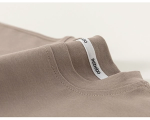 Detailed macro view of the crew neck and the branded white tape on the beige cotton T-shirt