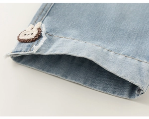 Vue détaillée du denim bleu clair avec un patch lapin tissé mignon et un ourlet effiloché usé