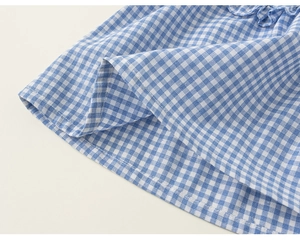 Detailed close-up of blue gingham fabric with delicate ruffled hem on girls' summer outfit
