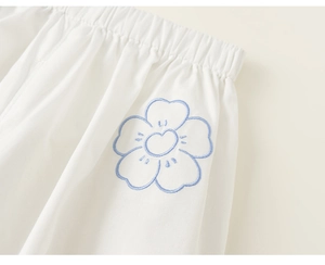 Detail shot of white kids pants featuring elastic waistband and blue flower embroidery