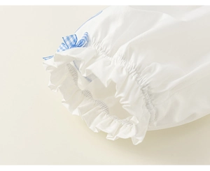 Detail of white cotton sleeve with elastic cuff, ruffles, and a blue plaid bow tie