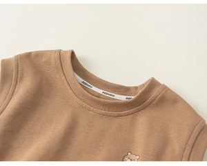 Close-up of light brown knitted toddler vest with ribbed neckline and bear embroidery