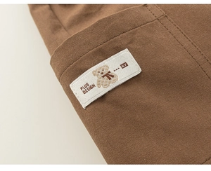 Close-up of brown cotton trousers with a white logo patch featuring a bear design