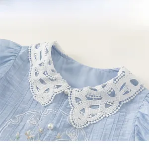 Detail of light blue girls' shirt featuring lace collar, floral embroidery and pearl buttons