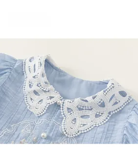 Close-up of light blue shirt featuring lace collar, pearl buttons, and floral embroidery