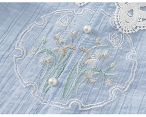 Detailed view of blue pleated fabric with floral butterfly embroidery and pearl buttons