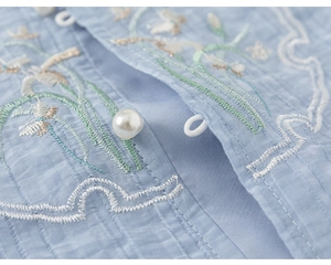 Macro view of blue summer blouse featuring delicate floral embroidery and a pearl button
