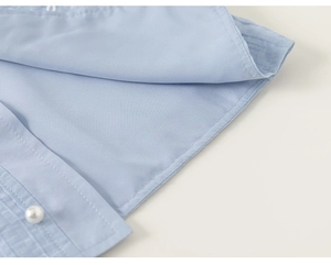 Close-up of light blue fabric texture and a pearl button on a girl's shirt