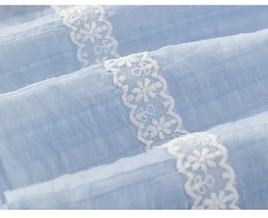 Detailed view of light blue pleated fabric with white floral lace embroidery details