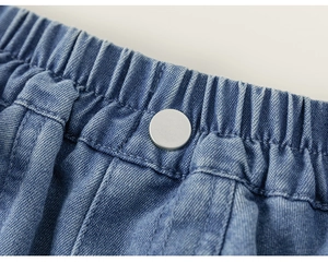 Detail of blue denim shorts showing elastic waistband and matte silver metal button