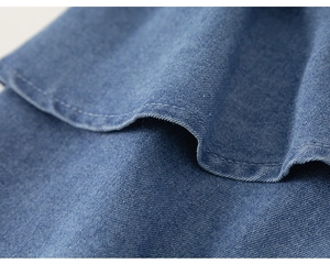 Detailed macro view of the ruffled hem and twin-needle stitching on blue denim fabric