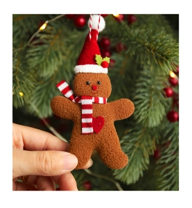 Detail of gingerbread man plush ornament with red scarf and hat held against Christmas tree