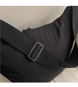 Detalle de la correa ajustable de nailon negro liso en un bolso bandolera de media luna