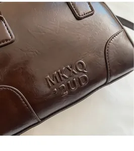 Close-up of dark brown leather texture with MKXQ 2UD embossed logo and fine stitching