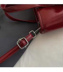 Close-up of premium silver-toned metal strap buckle on red patent leather handbag