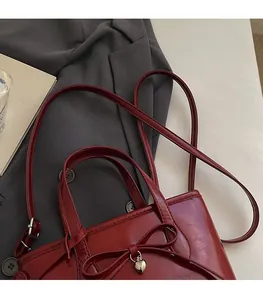 Detail of red leather tote bag with a bow, heart pendant, and adjustable shoulder strap