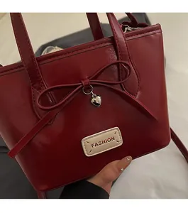 Close-up of red leather bucket bag featuring a bow, silver heart pendant and fashion label