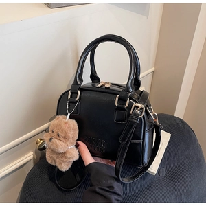Detail of black bowling bag with leather texture, MKXQ STUD logo, and plush bear charm