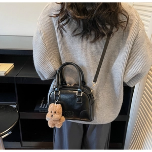 Detail of black glossy handbag with gold zipper and brown plush bear charm accessory