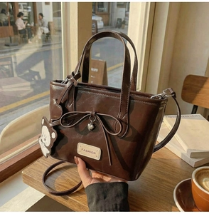 Detail der dunkelbraunen Leder-Eimertasche mit Schleifendeko und Bärenanhänger