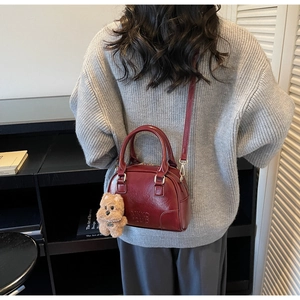 Detail of burgundy Boston bag with embossed logo and a cute brown plush bear charm