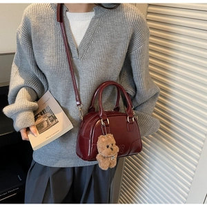 Detail of burgundy glossy leather handbag with bear charm on a model in soft light