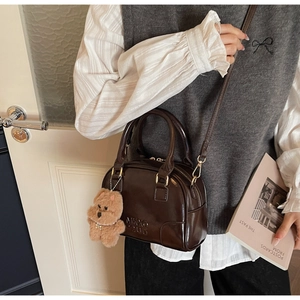 Detail view of brown leather Boston bag with teddy bear charm and adjustable strap