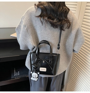 Detail of glossy black patent leather crossbody bag with heart charm and bear pendant