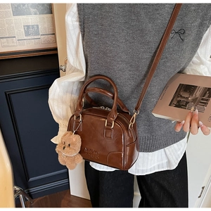 Brown glossy leather bowling bag with cute plush bear charm shown on a crossbody model