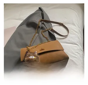 Detalle del bolso tote marrón vintage con cadena de metal y colgante de peluche sobre tela