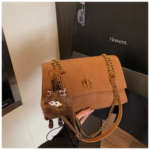 Detalle del bolso camel con cadena dorada y colgante de peluche de un monstruo