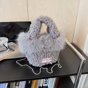 Gros plan d'un sac à main gris en peluche sur un bureau avec bandoulière chaîne et étiquette