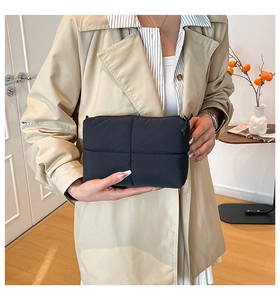 Detail of minimalist black quilted clutch bag held by model in a cozy indoor setting