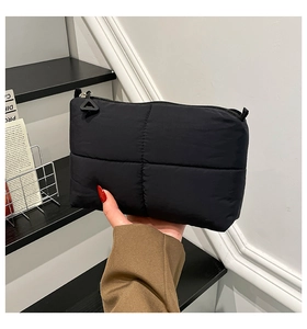Close-up of black quilted nylon clutch featuring a unique triangle zipper pull and padded texture