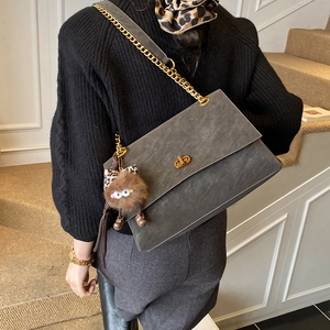 Vista de modelo de un bolso bandolera de ante gris oscuro con cadena dorada y colgante de peluche