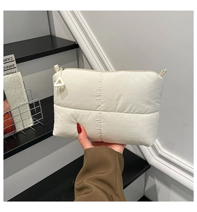 Detail of white quilted nylon clutch bag with minimalist triangular zipper puller