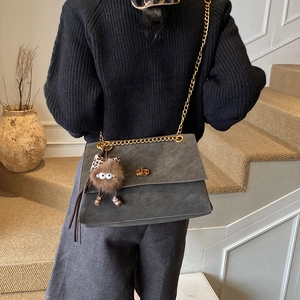 Detalle de bolso bandolera de ante gris con cadena dorada y colgante de peluche