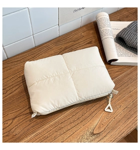 Detailed macro shot of cream quilted nylon clutch with triangle zipper on wood table