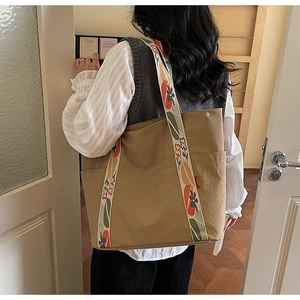 Détail d'un sac cabas kaki avec bandoulière brodée de fleurs dans un décor intérieur