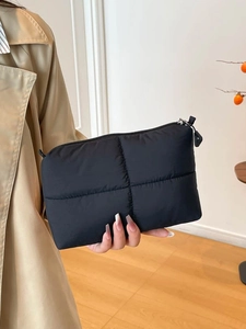 Minimalist black quilted puffer clutch bag with zipper closure held by model