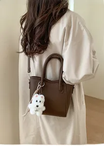 Détail du sac à bandoulière marron en cuir avec un joli charm de chien en peluche blanc