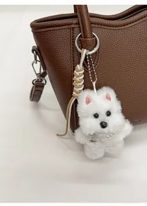 Détail d'un charme de sac chien en peluche avec collier de perles sur un sac en cuir
