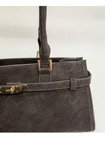Detail van een vintage grijze leren onderarmtas met een gouden metalen draaisluiting