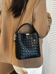 Chic black woven bucket bag with gold hardware worn by a model in a camel blazer