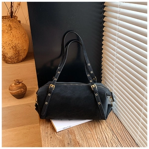 Detail view of black faux leather barrel bag with gold eyelets in a minimalist interior