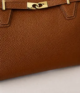 Macro shot of brown pebble grain leather tote bag with elegant golden metal twist lock