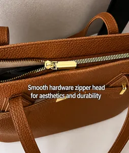 Detail of caramel brown lychee leather tote with gold zipper and reinforced stitching