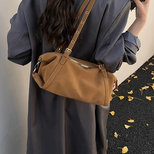 Detailed view of a brown suede cylinder shoulder bag with adjustable metal eyelet straps