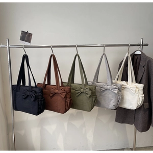 Detail showing five colors of large capacity tote bags with bow decoration on a rack